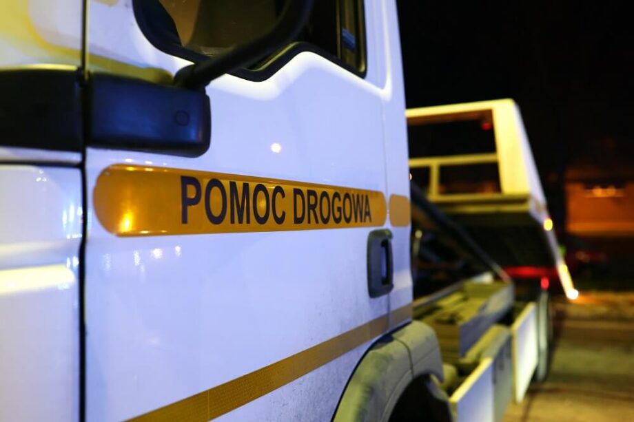 Ciężarówka z napisem "pomoc drogowa 24h" na boku, gotowa do działania w nocy.